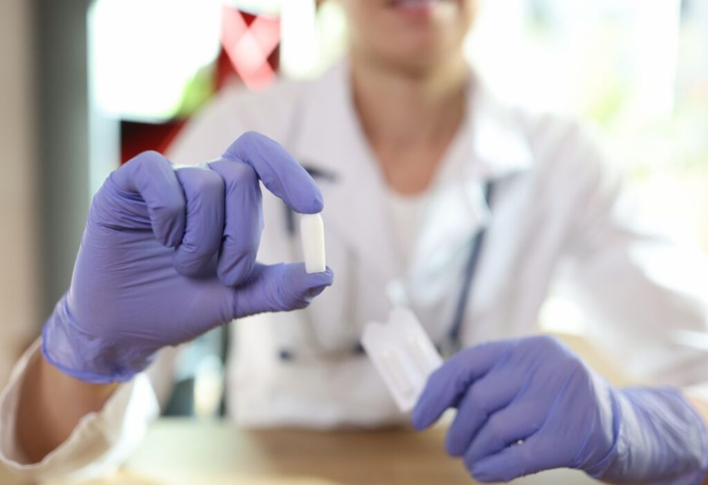 imagem de uma pessoa vestida de branco e com luvas roxas segurando um medicamento
